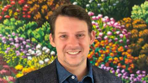 A young man with dark hair standing in front of a painted mural of flowers.