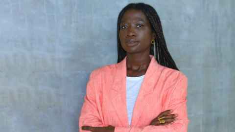 A young African woman wearing a peach jacket, white t-shirt and gold jewellery.