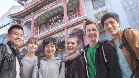 A group of young people in front of an ornate building with red columns.