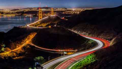 A nighttime view of hills, the Golden Gate bridge and city lights in the distance.
