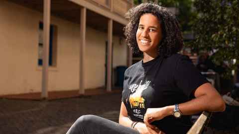 Melissa Irvine sitting in front of the Humanities Building / Te Puna Aronui