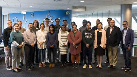 Group of people standing and smiling facing the camera with a blue wall behind them.