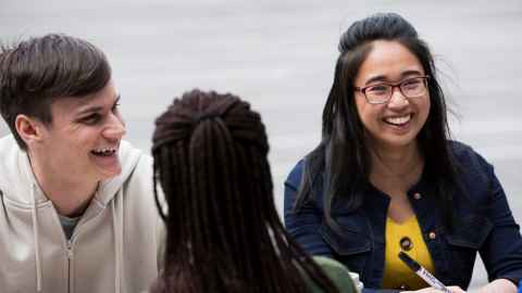 Three students sitting outside. two are facing camera and smiling