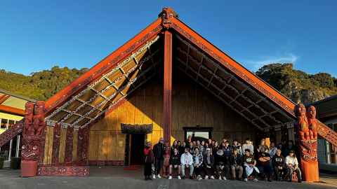 A group of students and teachers standing in front of a marae.