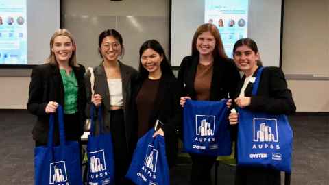 Five smiling students holding branded tote bags