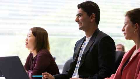 Three smiling people sitting at a desk.