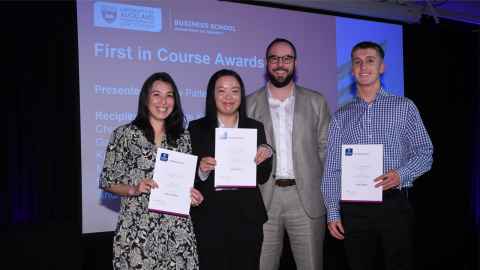 Two young women and a young man holding certificates and flanking an older man