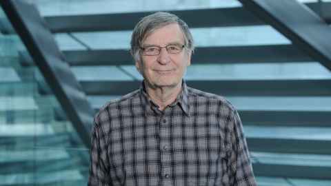 A smiling older man with glasses and wearing a checked shirt