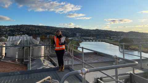 A smiling young woman wearing a hi-vis vest and hard hat on the rooftop of a building
