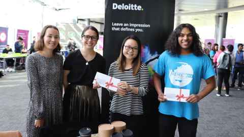 Four people, smiling, by a Deloitte sign at an event in the Business School.