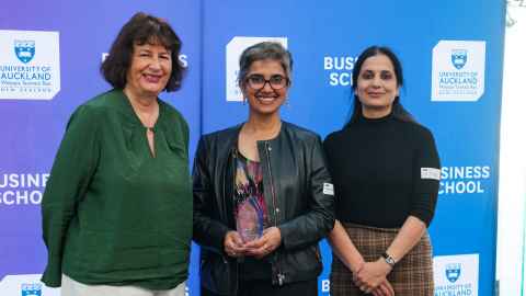 Three smiling women in front of a Business School backdrop.