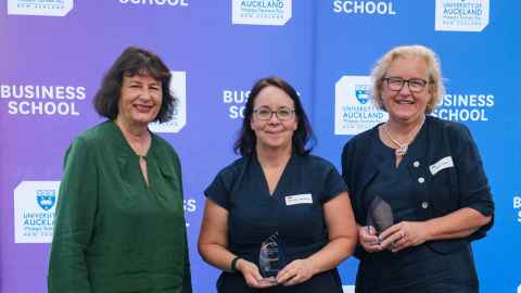 Three smiling women in front of a Business School backdrop.