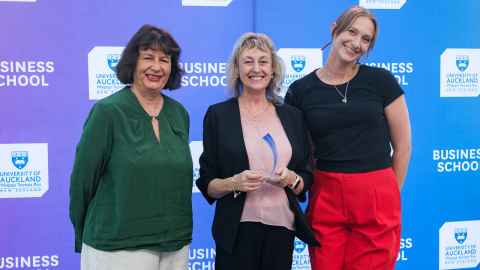 Three smiling women in front of a Business School backdrop.