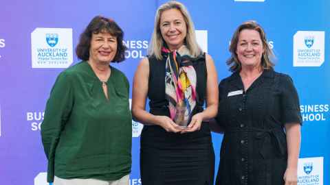 Three smiling women in front of a Business School backdrop.