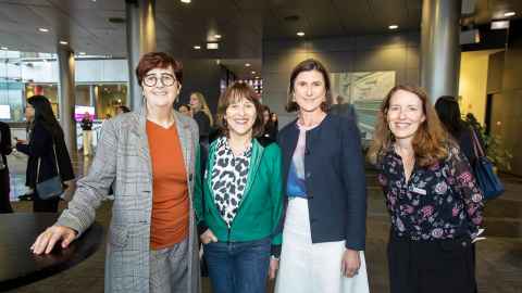 Group of four women standing together, smiling.