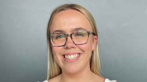A smiling young woman with blonde hair and glasses