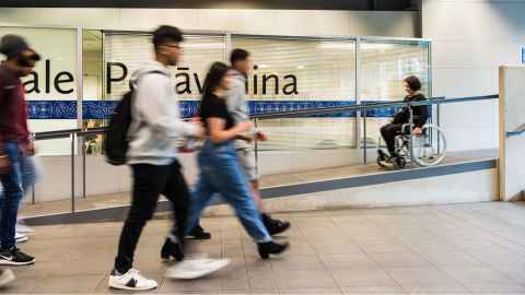 People walking indoors, with one person using a wheelchair on an accessible ramp.