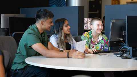 Group of three students sitting at a table looking at a computer.