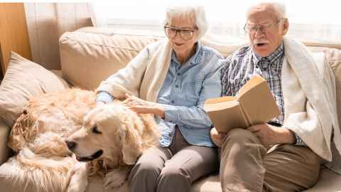 Two elderly people on a sofa with a dog.