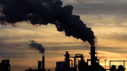 Black smoke pouring out of industrial chimneys as the sun sets.