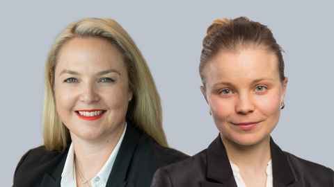 Two women wearing black blazers and white blouses.