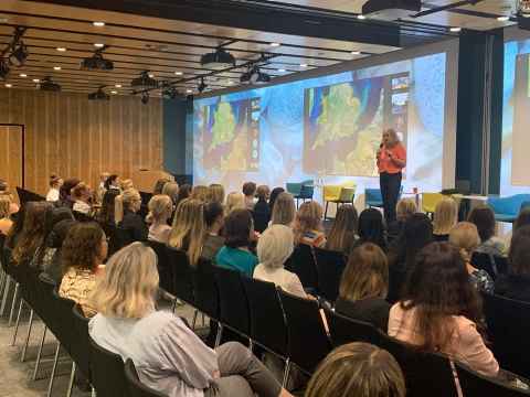 A woman on a stage, speaking to a group of women.