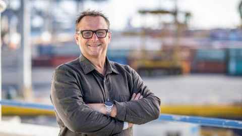 A smiling man, wearing glasses, with arms crossed