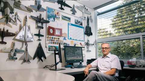 A man in an office with one wall covered in models of military planes.