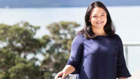 Nicole stands smiling on a balcony, with an ocean view in the background