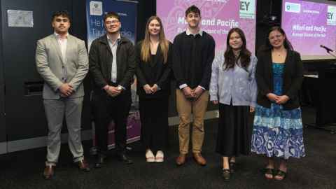 Group of six students standing in a row in front of digital screens.
