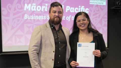 A smiling young Pacific woman holding a certificate and standing next to another man
