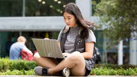 Young woman sitting outside on the grass looking at her laptop.