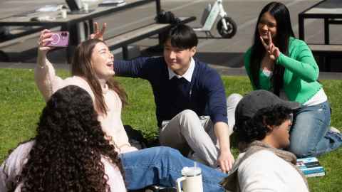 Group of four students sitting at a table looking at a laptop.