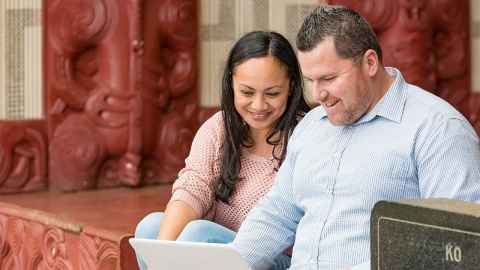 a man and woman looking at laptop in front of a marae