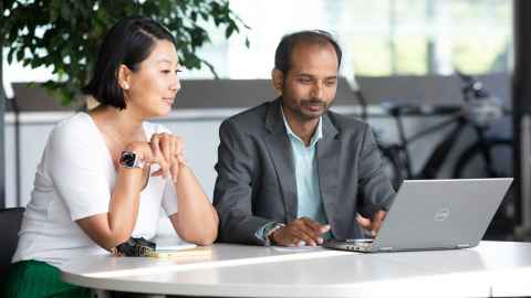 A man and a woman sitting at a table looking at a laptop at the university of Auckland business school.