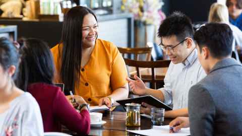 Four students around a table, discussing and smiling