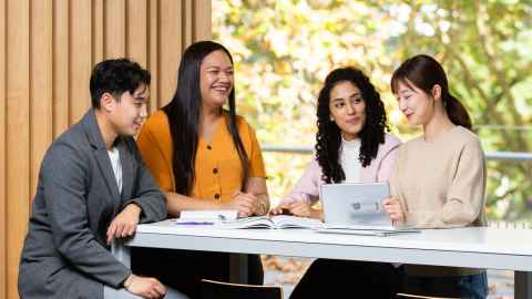 Four students seated around a study table with notebooks and a laptop