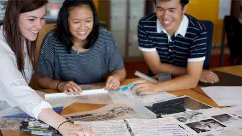 Three students talking at a table over study materials 