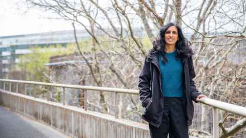 Kavita standing on balcony in front of trees and city scape.