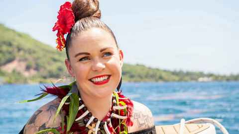 Tyla smiles with a red hibiscus in her hair, with the ocean in the background