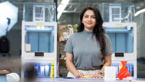 Close up of Riya standing the Design Fabrication Lab in front of 3D printers