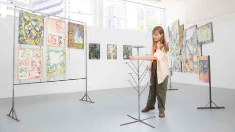 Georgia placing a small sculpture on a display stand for her exhibition, with her paintings in the background.