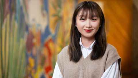 Student smiles politely at camera, artwork is behind her but it is blurred