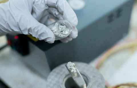 Someone wearing gloves, handling a substance from a glass vial.