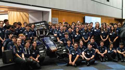 A group of students with a racing car in the Engineering building.