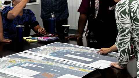 A group of people working over a poster of work on a big table
