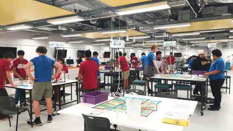 A room full of young people standing around tables.