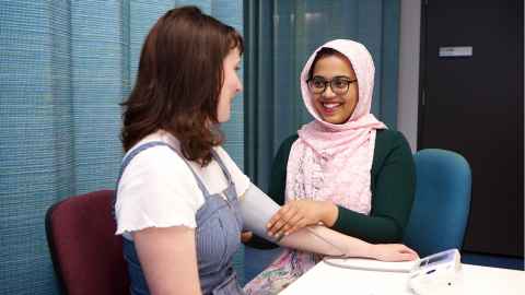 A smiling young woman taking another young woman's blood pressure.