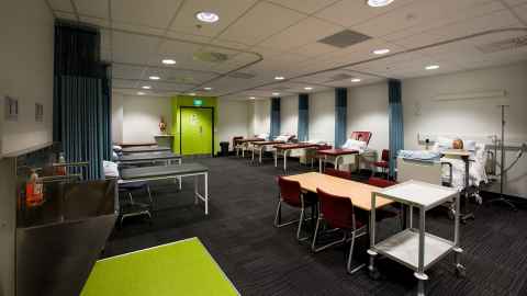 A large room with tables, chairs and hospital beds.