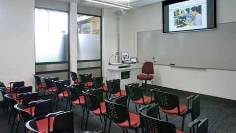 A room with a lectern, whiteboard, screen and rows of chairs.